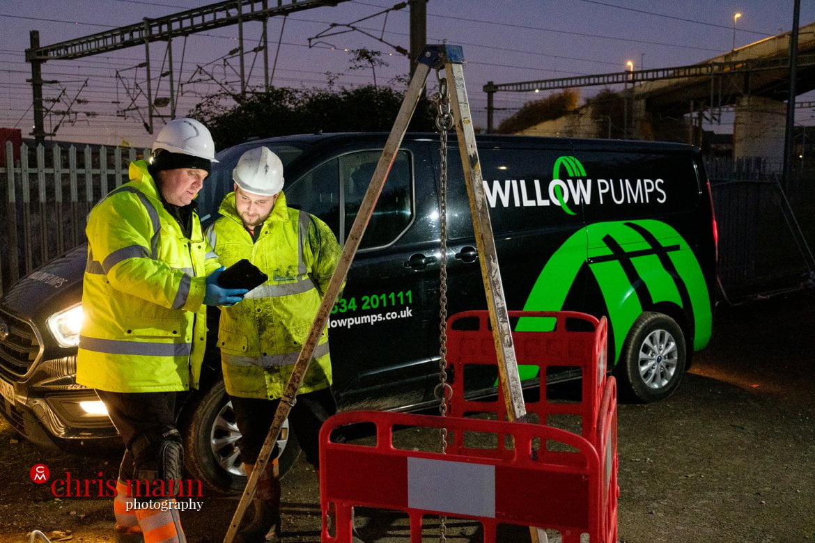 Willow Pumps engineers confer next to a drainage access point in this twilight photo